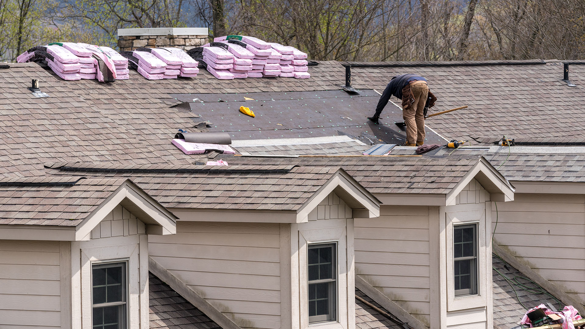 A working on a roof is installing asphalt shingles.