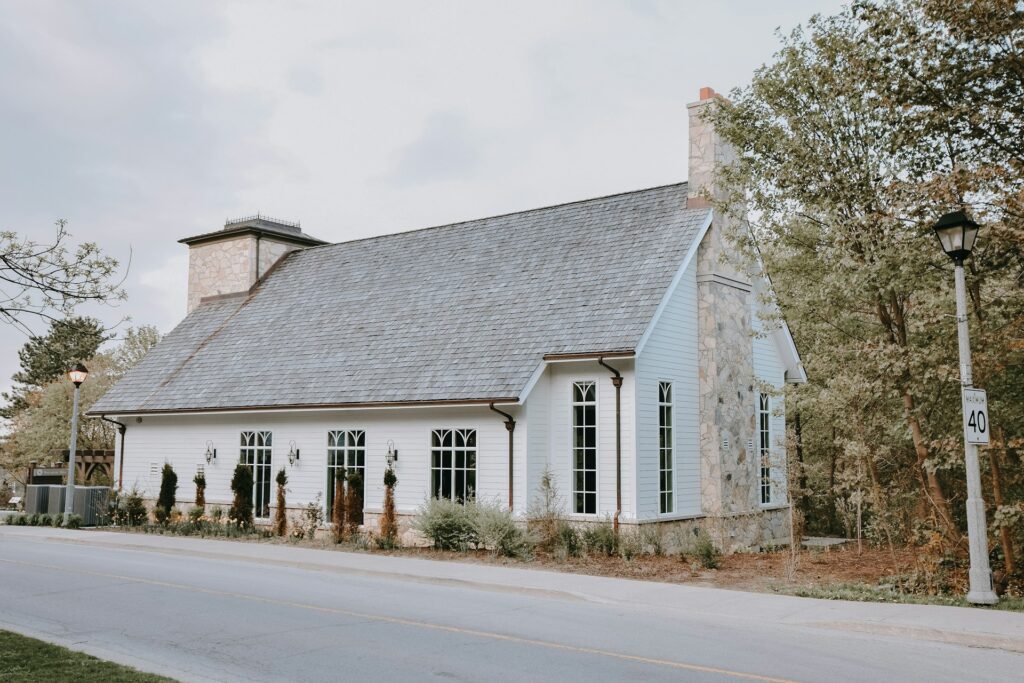 A white building with a stone chimney and arched windows, set amid trees, sits beside a road with a 40 km/h speed limit sign.
