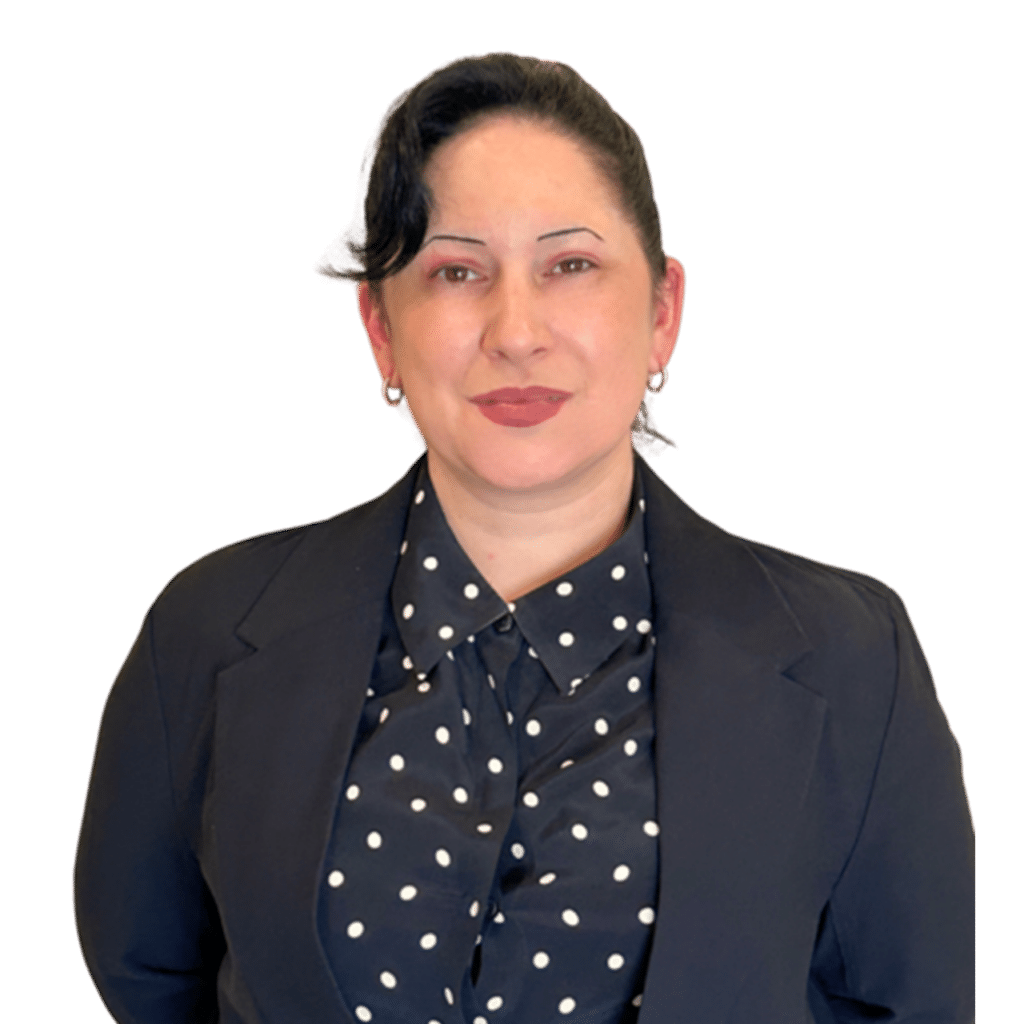 Woman with dark hair in a bun, wearing a black blazer over a black blouse with white polka dots, standing and looking at the camera with a neutral expression.