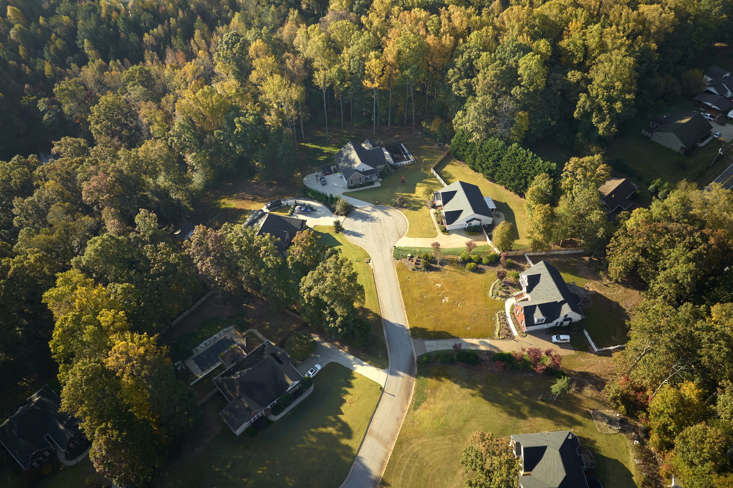 Aerial view of a suburban cul-de-sac surrounded by trees, with several houses, driveways, lawns, and a curved road.