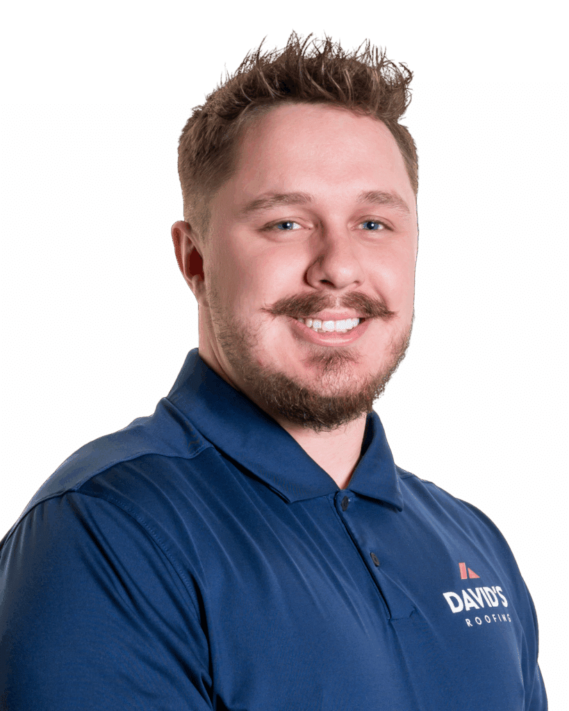 A man with short hair and a beard smiles, wearing a navy blue polo shirt with the “DAVID’S ROOFING” logo on it, standing against a plain white background.