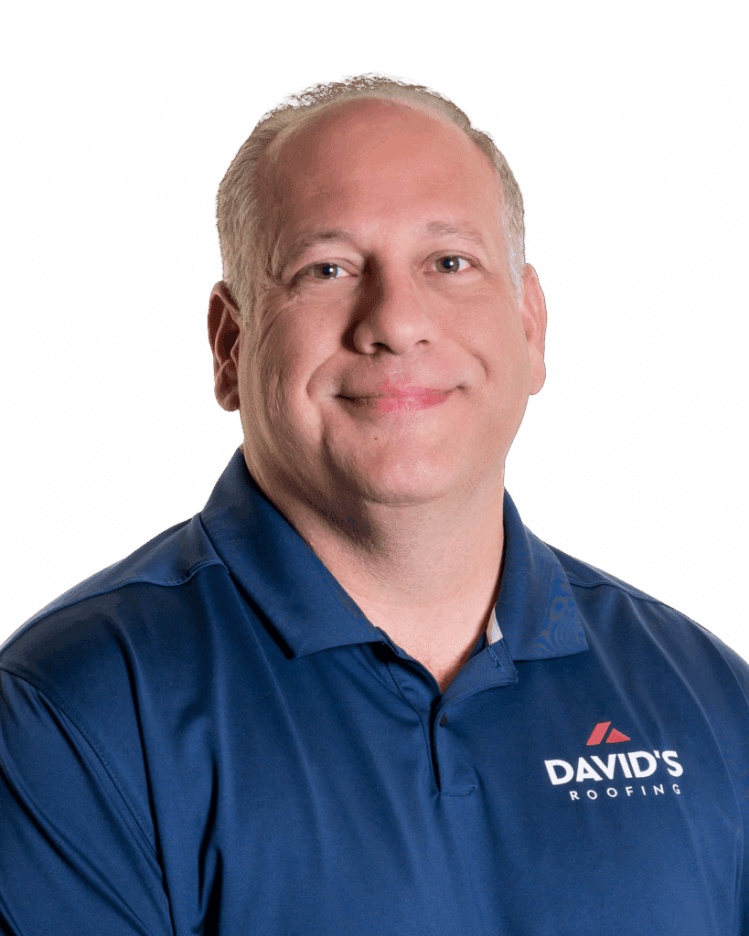 David's Roofing General Manager, a middle-aged man with short light hair wearing a blue polo shirt with "David's Roofing" logo, smiling at the camera against a plain white background.
